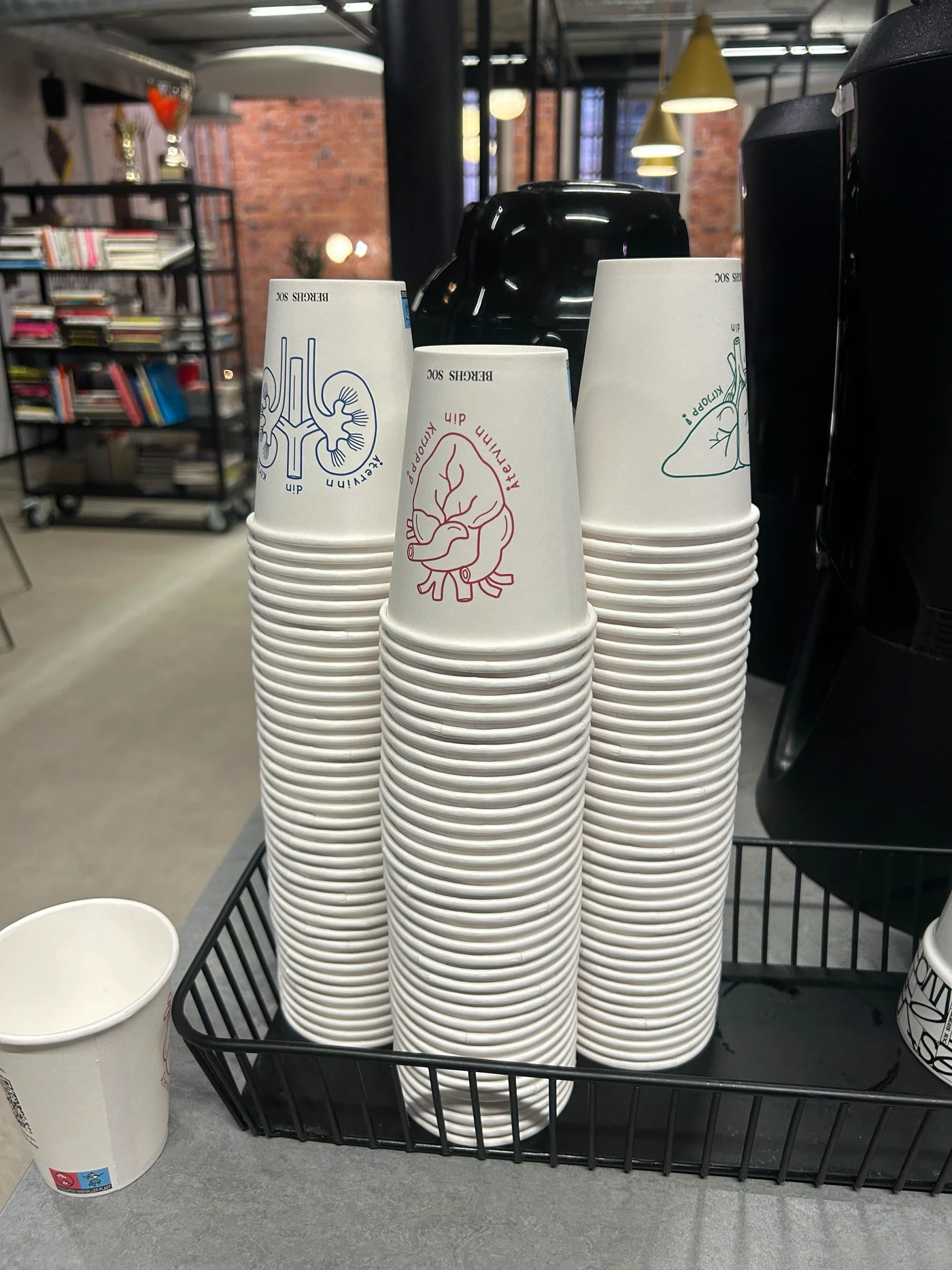 Stacks of the liver, heart and kidney campaign cups beside a coffee machine at Berghs.
