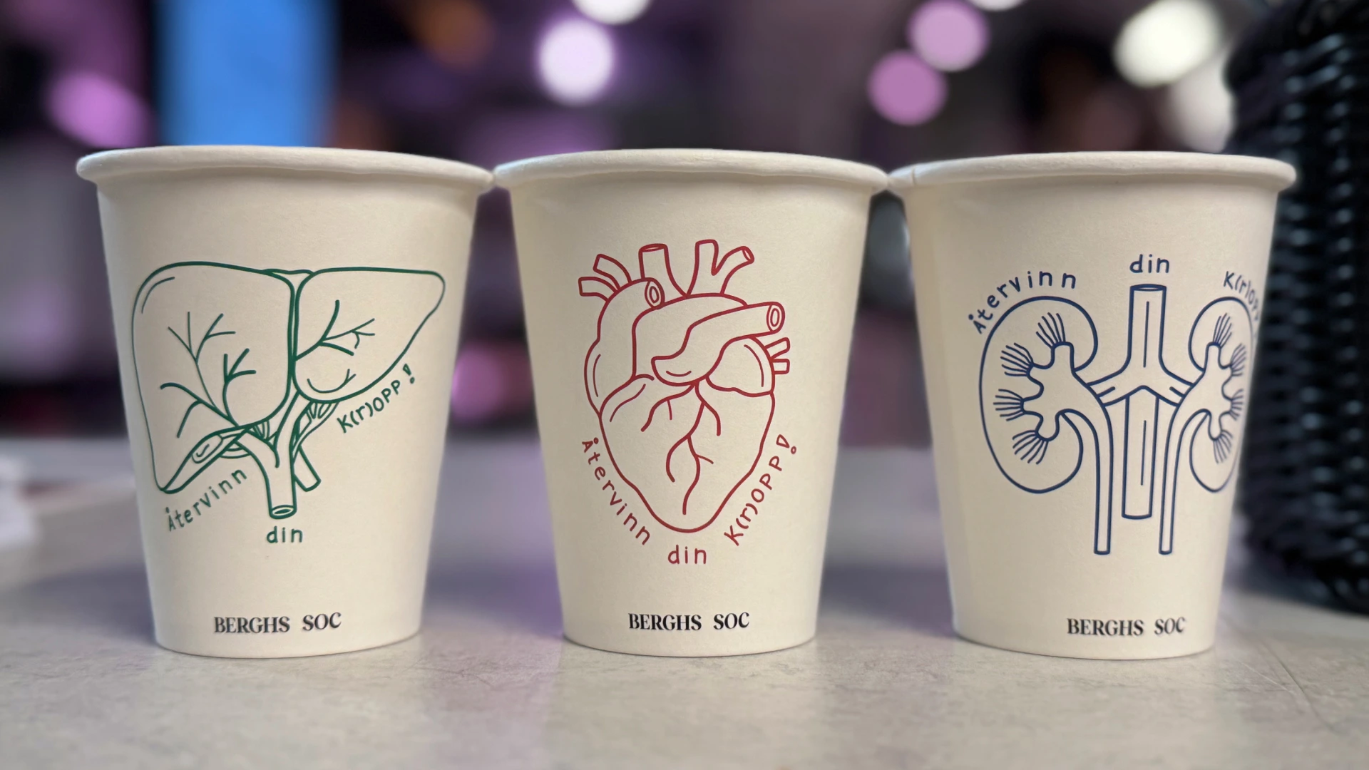 Three printed Berghs coffee cups with green liver, red heart and blue kidney illustrations.